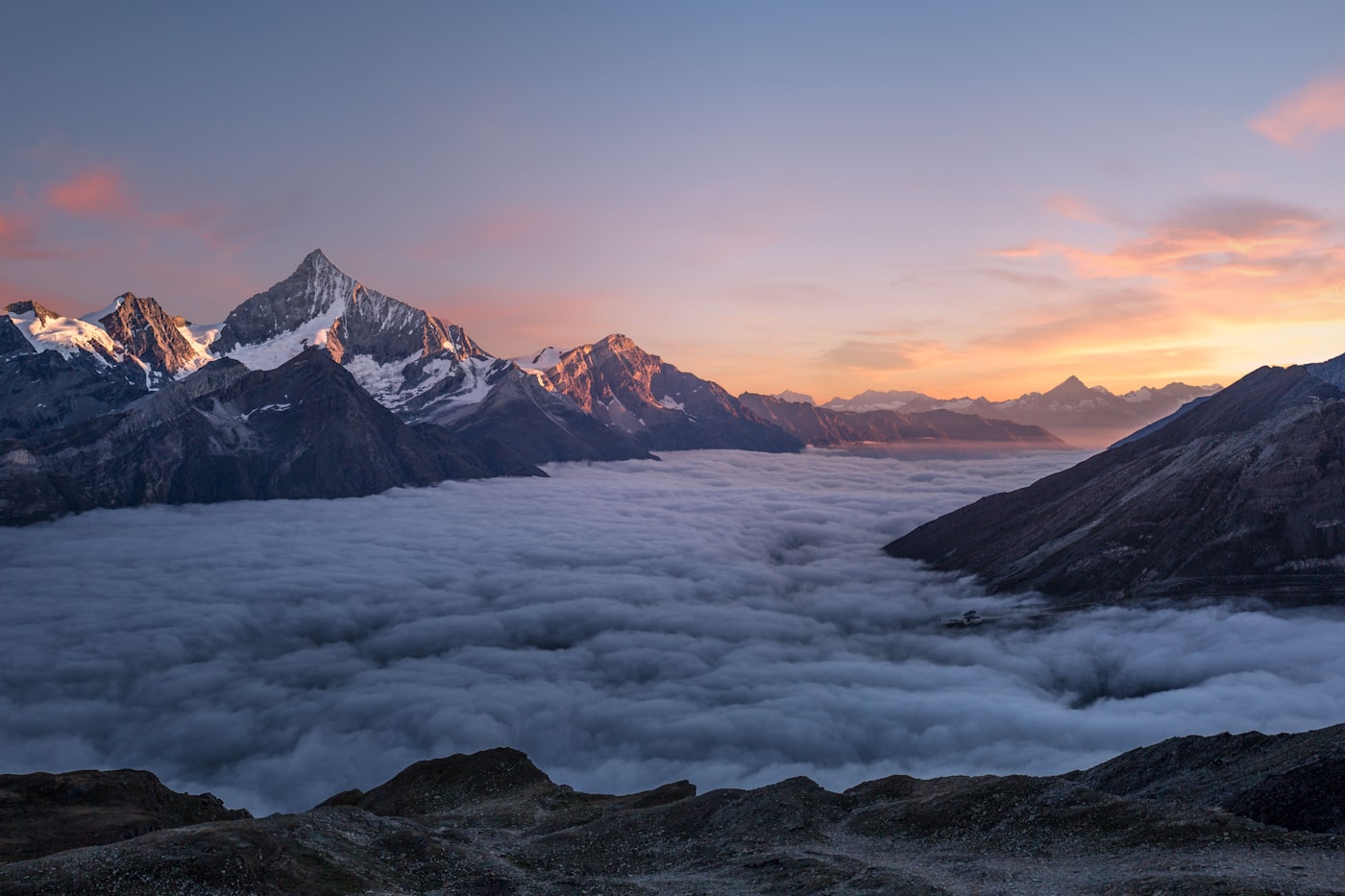 Color photograph of snow-capped mountain peaks rising above a sea of clouds at sunset